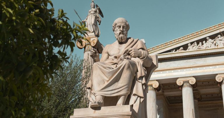 Plato's statue in front of the National Library of Greece against a clear blue sky.