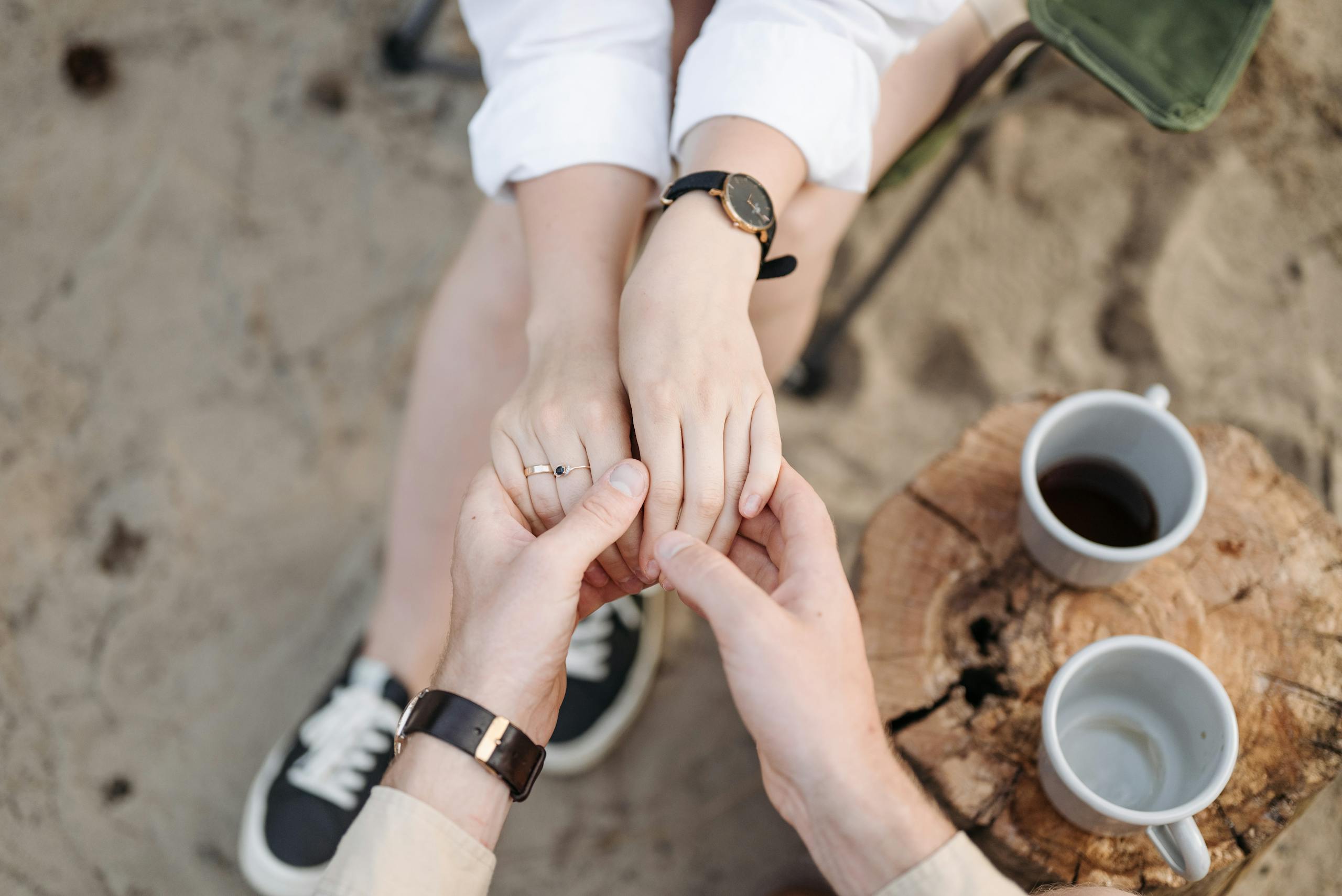 A couple's hands held gently, symbolizing love and connection. Outdoors with coffee cups and a rustic setting.