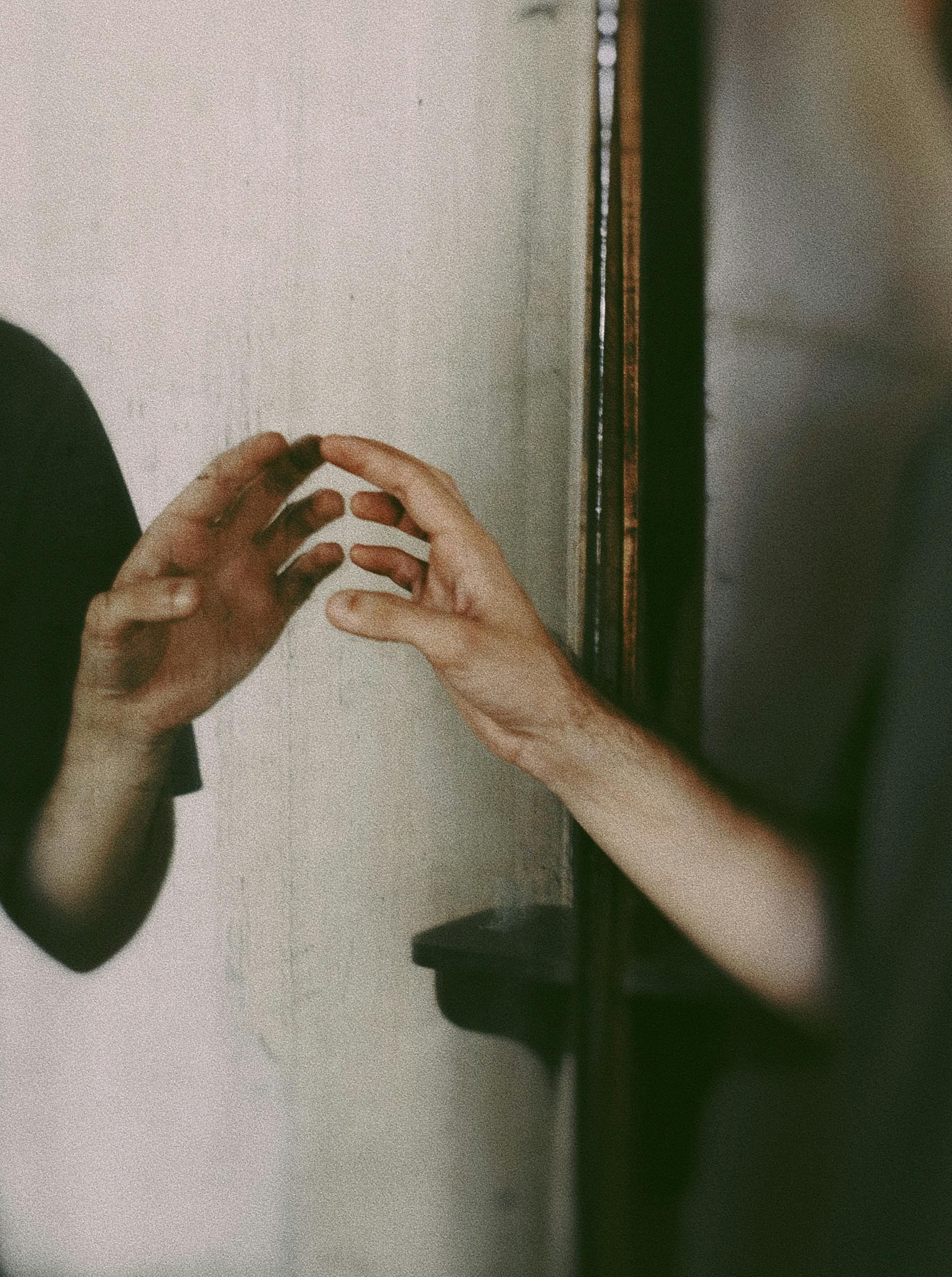 A person's hand reaching towards its reflection in a mirror, creating a mysterious mood.