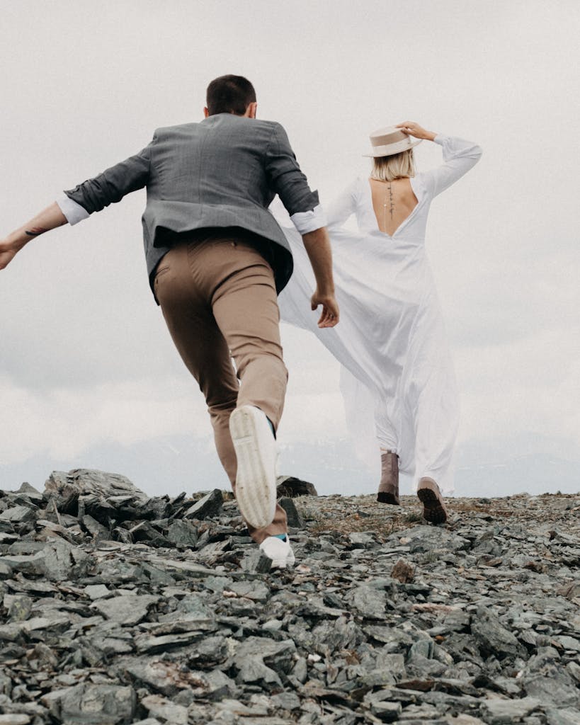 Couple running on rocky terrain in wedding attire, capturing dynamic love and adventure.