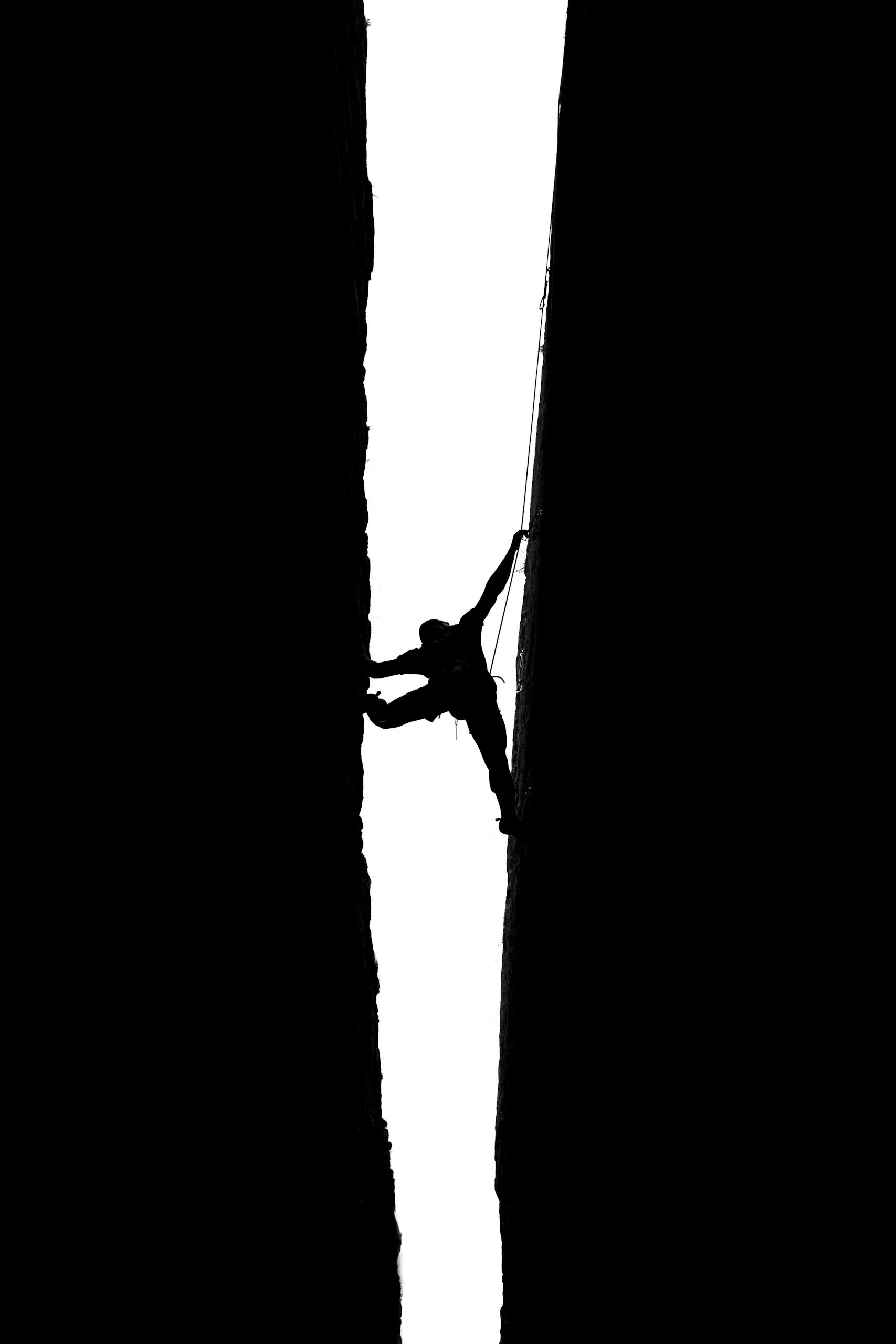 Dramatic silhouette of a climber scaling Pennadomo's narrow rock crevice, showcasing strength and balance.