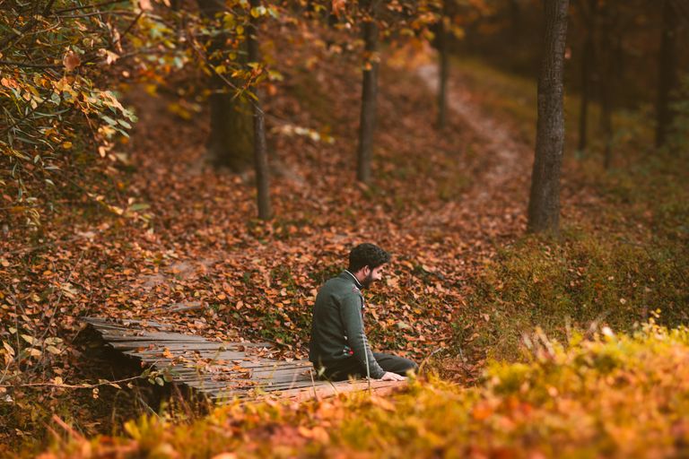 A man sitting alone on a wooden path in an autumn forest setting.