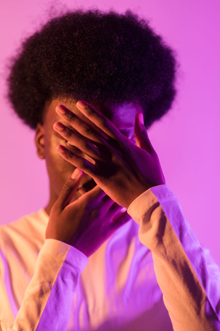 A creative portrait of a man with face covered by hands, bathed in purple light.