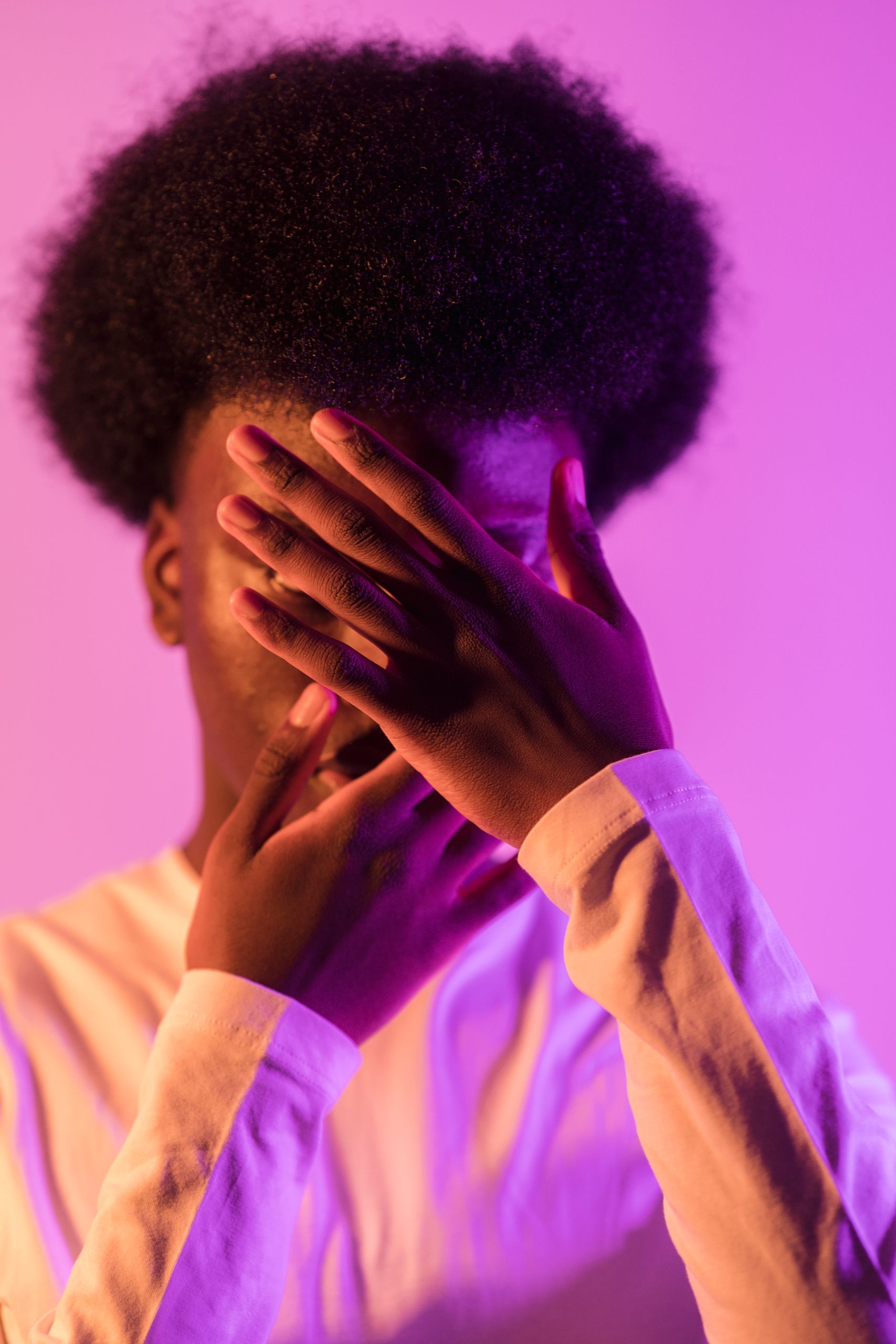 A creative portrait of a man with face covered by hands, bathed in purple light.