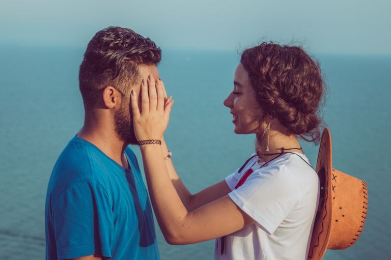 Joyful couple playing peekaboo outdoors by the sea, capturing a playful moment.